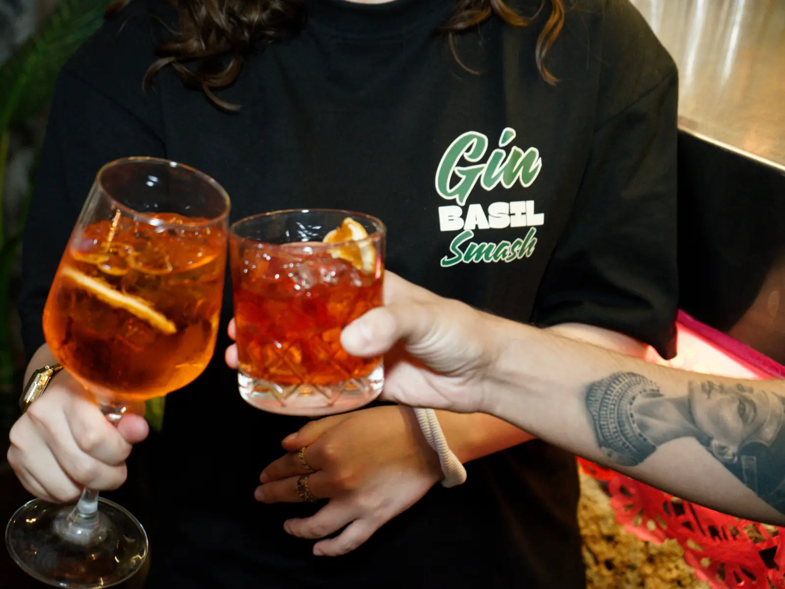 Dos personas brindando en la barra con playeras The Last Drop